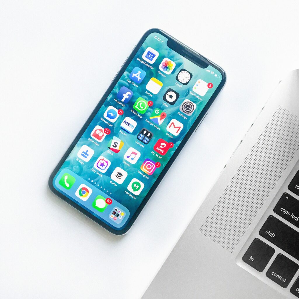 A mobile phone with lots of apps next to a laptop.