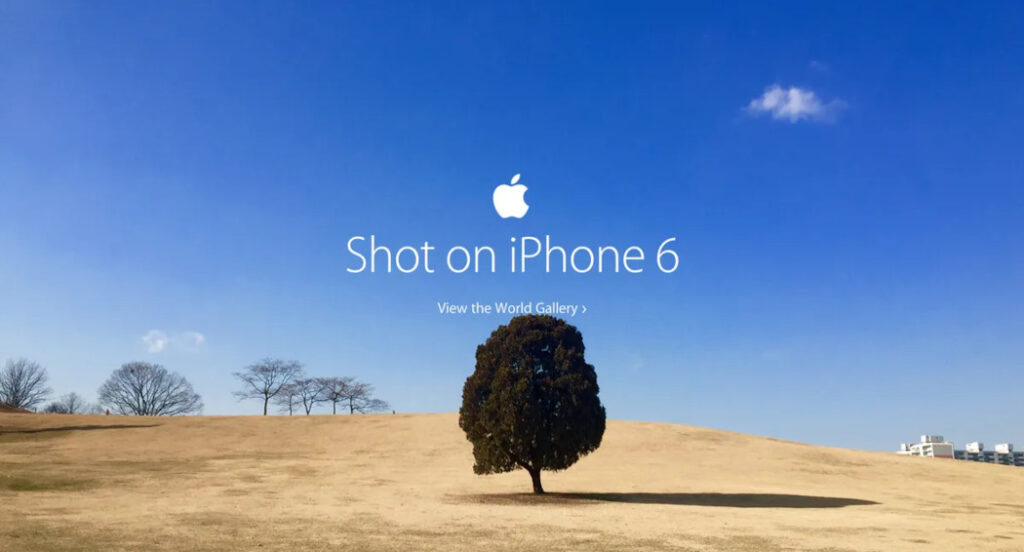 Ad per Iphone 6. Immagine di un albero in mezzo a un paesaggio di terra ambrata con il cielo azzurro. Il claim recita: "Shot on Iphone 6".